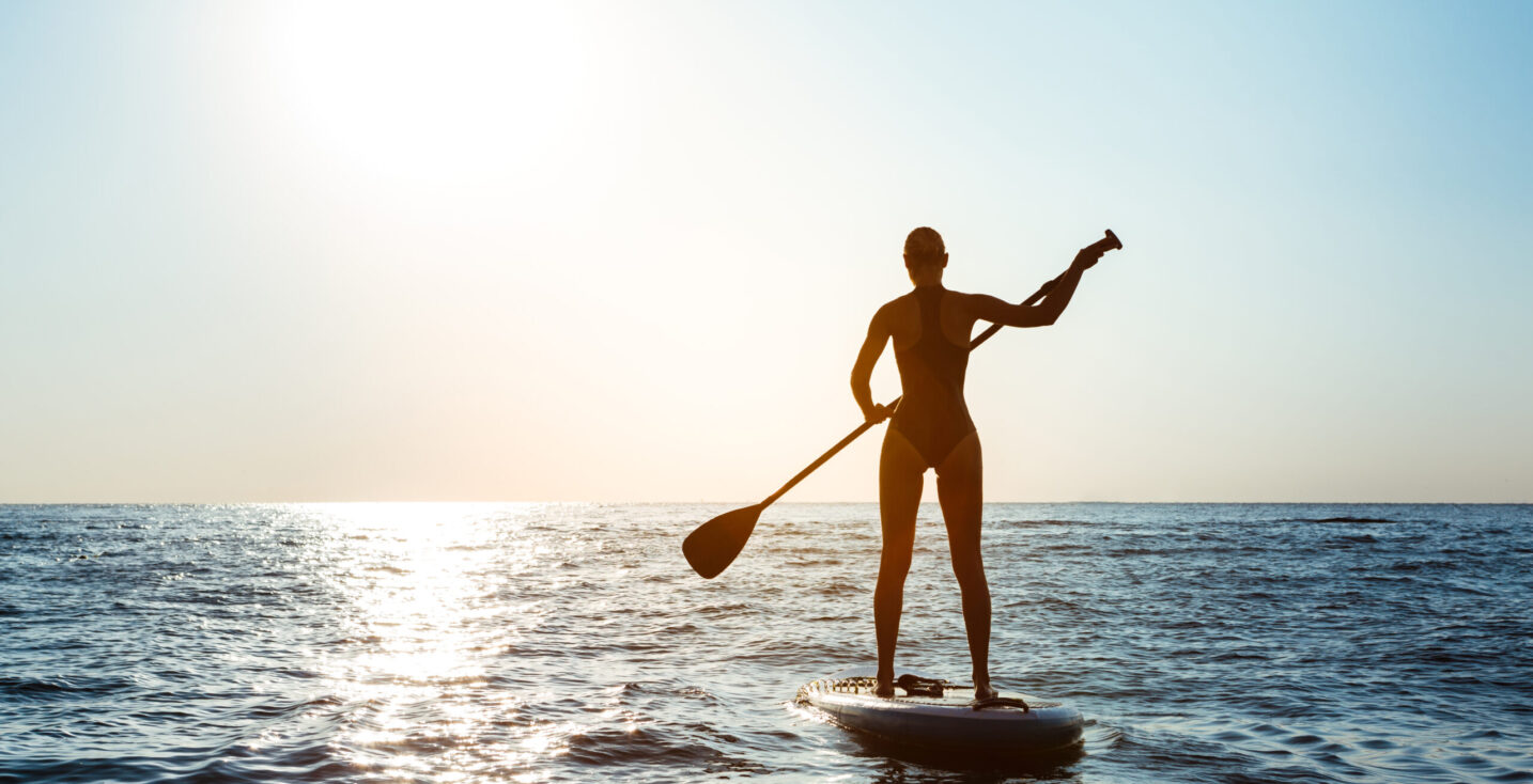 Silhouette of young beautiful girl surfing in sea at sunrise. Outdoors.